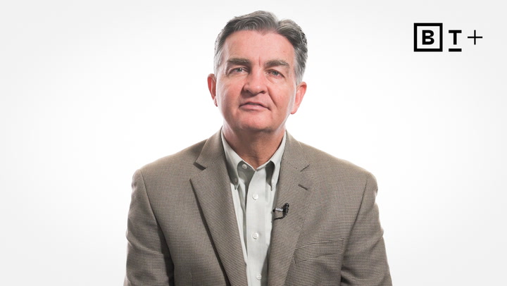 A man in a brown blazer and light shirt sits against a plain white background with a "BT+" logo in the top right corner.