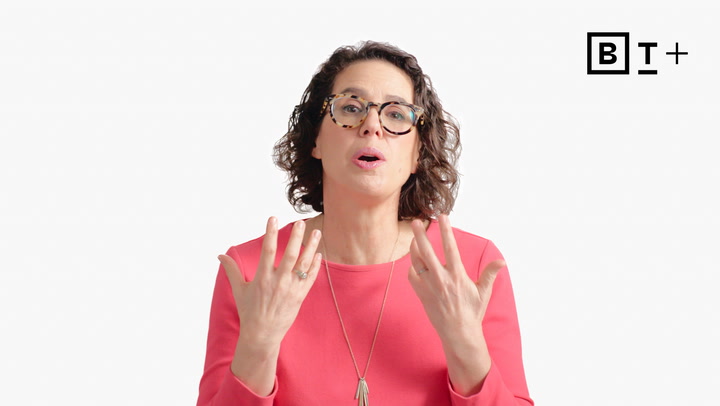 A woman with curly hair and glasses, wearing a pink top and a long necklace, gestures with both hands against a plain white background with a "BT+" logo in the top right corner.