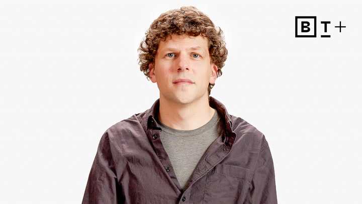 A man with curly brown hair wearing a gray t-shirt and dark button-up shirt stands against a white background with a "B T +" logo in the top right corner.