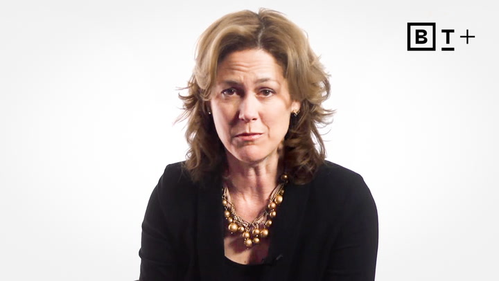 A woman with shoulder-length brown hair wearing a black top and gold necklace sits in front of a white background with a "BT+" logo in the top right corner.
