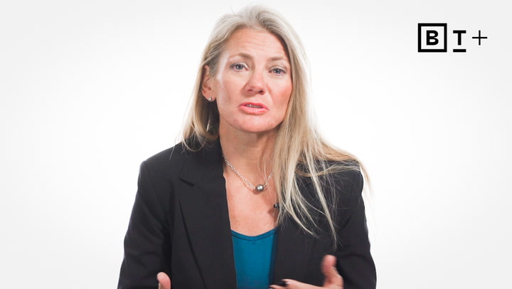 A woman with long blonde hair, wearing a black blazer and teal top, speaks in front of a plain white background with a "B T +" logo in the top right corner.