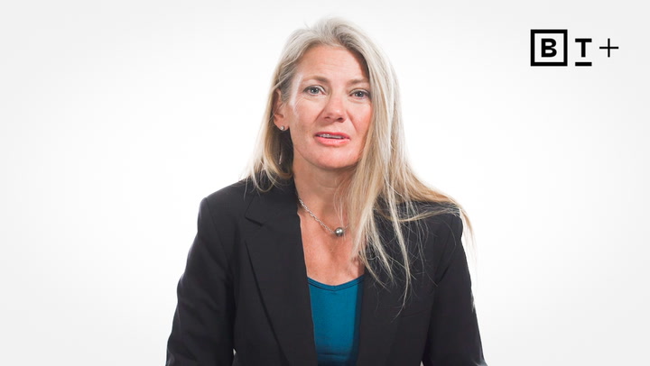 A woman with long blonde hair wearing a black blazer and blue top sits against a white background with a BT+ logo in the top right corner.