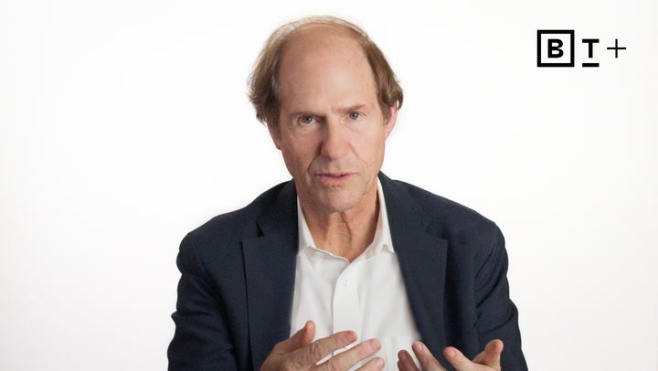 A middle-aged man with thinning hair, wearing a dark blazer and white shirt, speaks against a plain white background with a "BT+" logo in the top right corner.