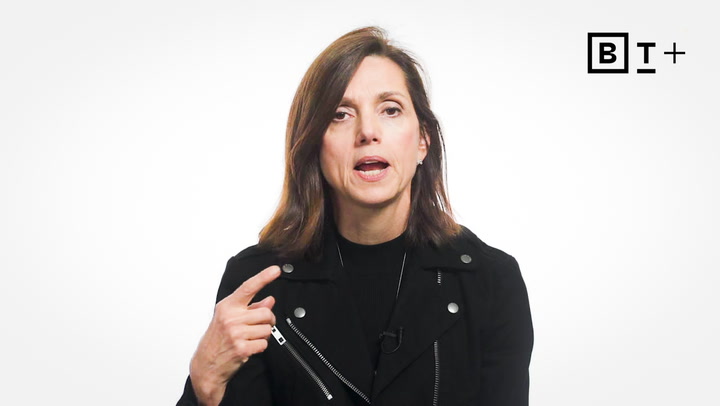 A woman with shoulder-length brown hair speaks while pointing to herself, wearing a black jacket against a plain white background with a "BT+" logo in the top right corner.