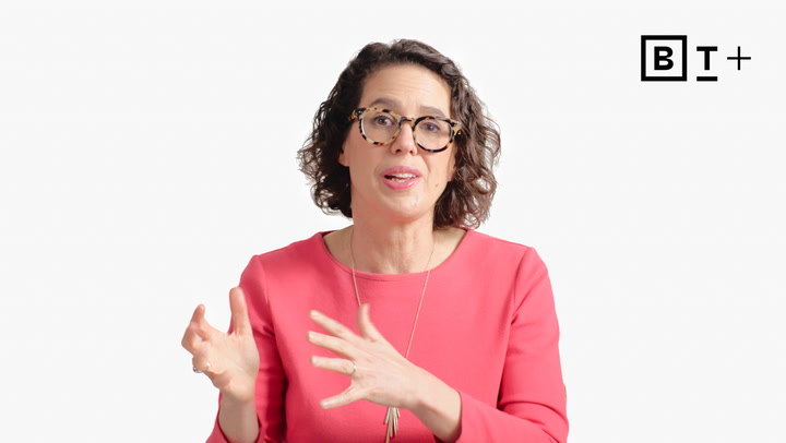 A person with curly hair and glasses, wearing a pink top, gestures with their hands while speaking in front of a plain white background with a "B T +" logo in the corner.
