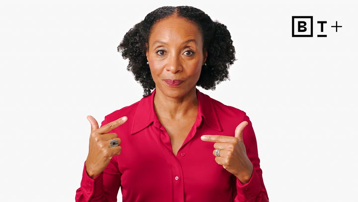 Woman in a red blouse points to herself with both hands, standing against a plain white background with a "BT+" logo in the top right corner.