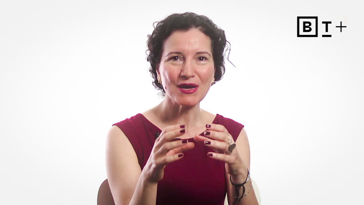 A woman with short curly hair in a sleeveless red top gestures with her hands while speaking, against a white background with a "BT+" logo in the corner.