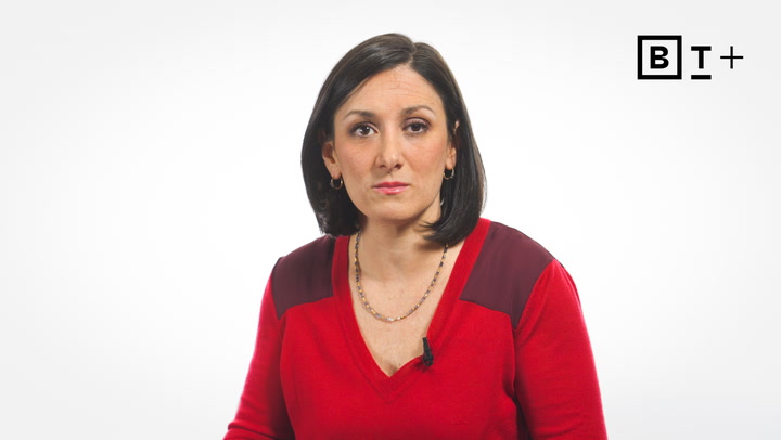 A woman with straight dark hair, wearing a red top and necklace, looks at the camera against a plain white background with a "BT+" logo in the upper right corner.