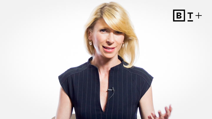 A woman with blonde hair in a dark pinstripe top speaks, gesturing with her hand. A microphone is clipped to her shirt. BT+ logo is visible in the top right corner.