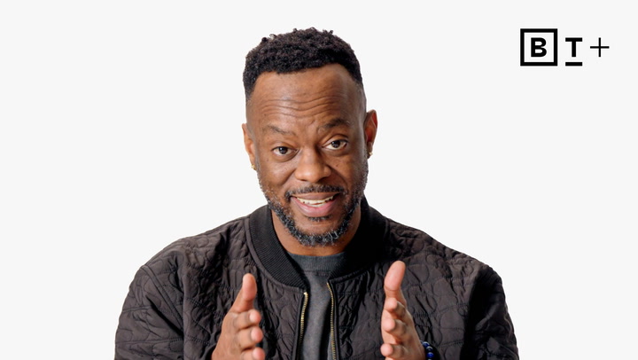 A man with a short beard and black jacket gestures with his hands, standing in front of a plain white background with a "B T +" logo in the corner.