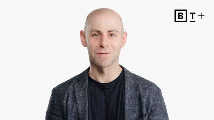 A bald man in a blazer and dark shirt faces the camera against a plain white background with a "BT+" logo in the corner.