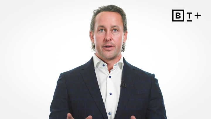 A man in a suit stands against a plain white background with the “BT+” logo in the top right corner.