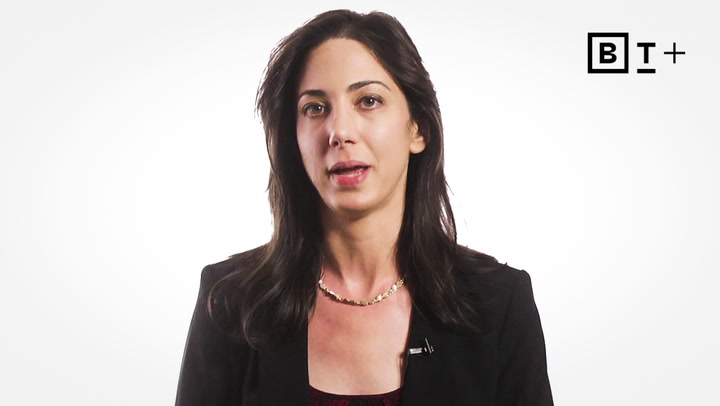 A woman with long dark hair wearing a black blazer and necklace speaks in front of a plain white background with a "BT+" logo in the corner.