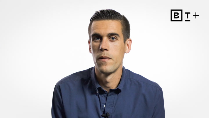 A man with short dark hair wearing a blue button-up shirt sits against a plain white background with the "BT+" logo in the top right corner.