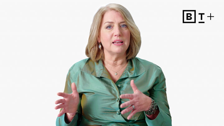 A woman with shoulder-length blonde hair in a green satin blouse speaks while gesturing with her hands. The BT+ logo is visible in the top right corner.