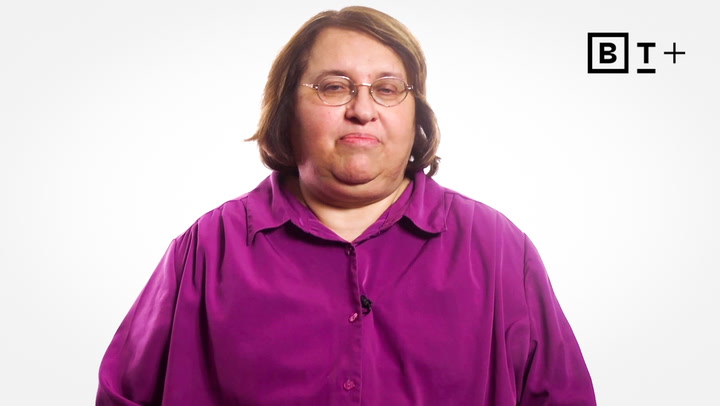 A person with short brown hair, wearing glasses and a magenta button-up shirt, stands against a plain white background with a "BT+" logo in the corner.