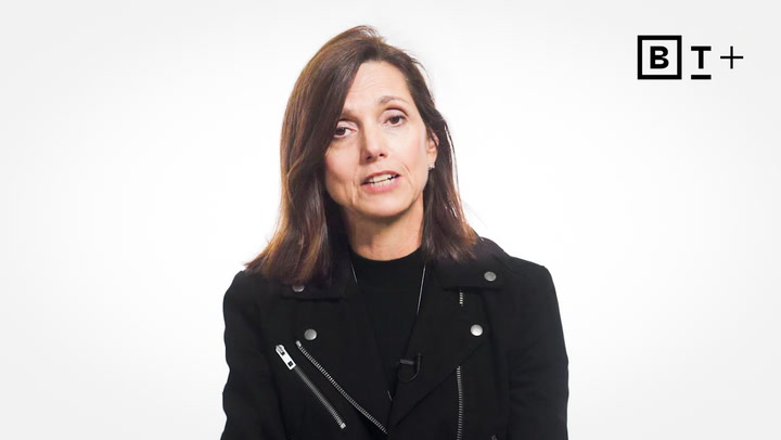 A woman with shoulder-length brown hair wearing a black jacket sits in front of a white background with a "BT+" logo in the top right corner.
