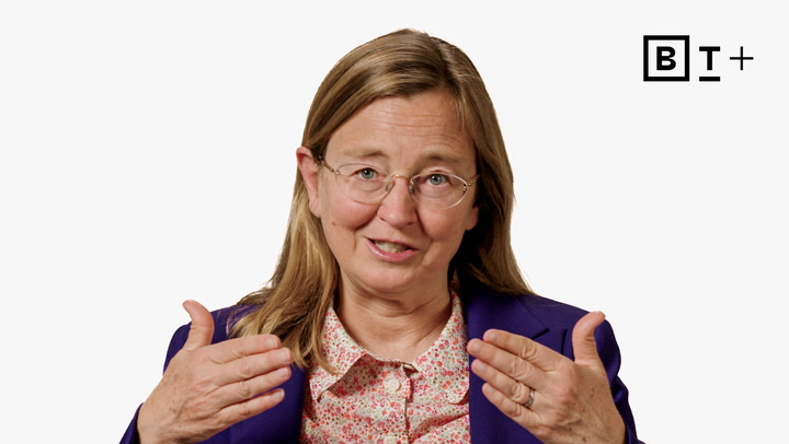 A woman with glasses and long hair, wearing a purple blazer and floral shirt, gestures with both hands. The "BT+" logo appears in the top right corner against a white background.