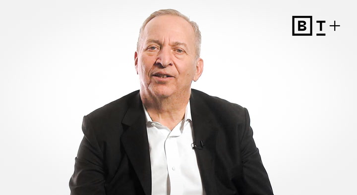 An older man in a black suit jacket and white shirt sits in front of a plain white background with the B+ logo in the top right corner.