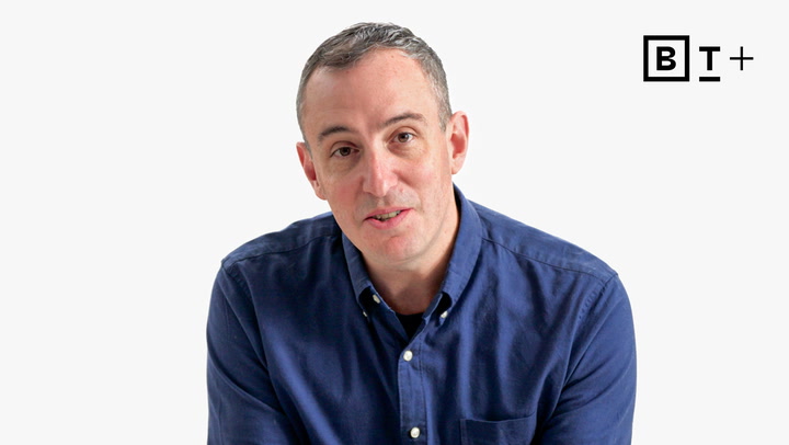 A man with short hair wearing a blue button-up shirt sits against a plain white background with a "B T +" logo in the top right corner.
