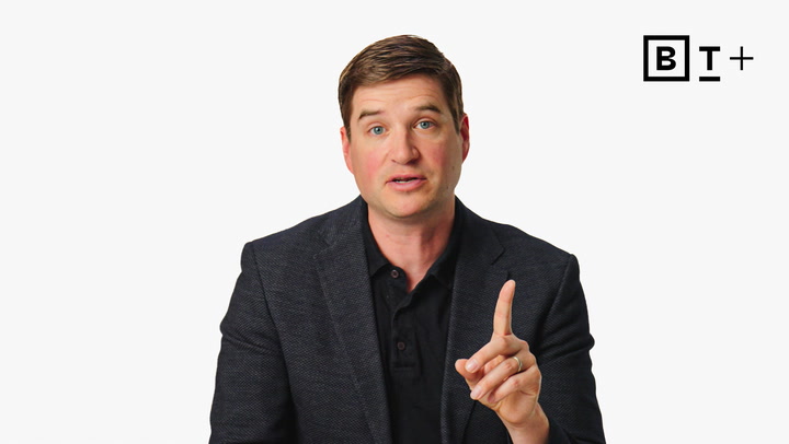 A man in a dark blazer sits against a white background, holding up his index finger. The BT+ logo is displayed in the top right corner.
