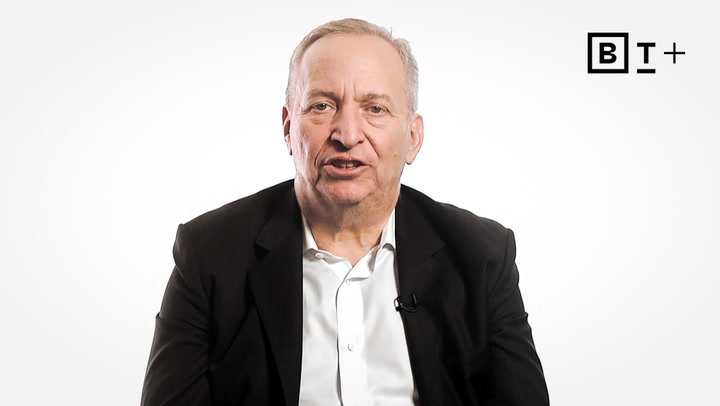 An older man in a black jacket and white shirt sits against a plain white background with a "B T +" logo in the top right corner.