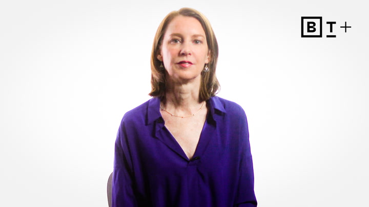 A woman with shoulder-length brown hair wearing a purple blouse sits in front of a white background with a "B T +" logo in the top right corner.