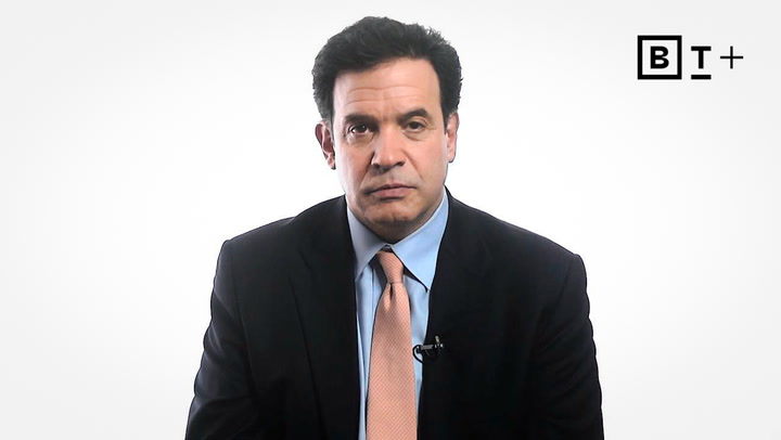 A man in a dark suit, blue shirt, and peach tie sits against a plain white background with a "BT+" logo in the top right corner.