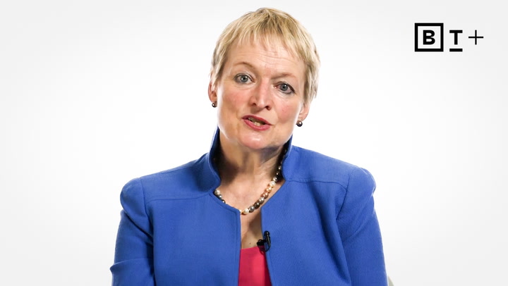A woman with short blonde hair wearing a blue blazer and pearl necklace speaks in front of a white background with a "BT+" logo in the corner.