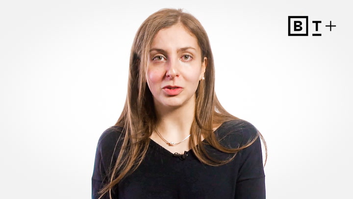 A woman with long brown hair wearing a black top speaks in front of a white background with a "BT+" logo in the top right corner.