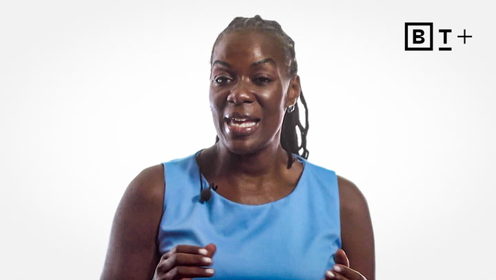 A person wearing a blue sleeveless top speaks while standing in front of a white background with a "BT+" logo in the top right corner.