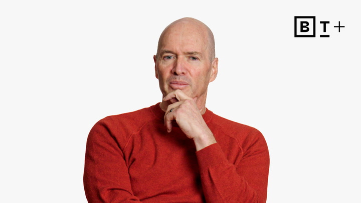 A man in a red sweater poses with his hand on his chin against a plain white background. The letters "BT+" appear in the top right corner.