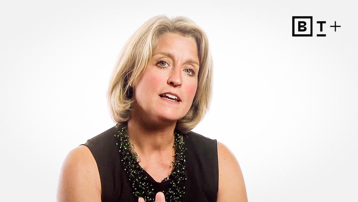 Middle-aged woman with short blonde hair wearing a black sleeveless top and beaded necklace, speaking against a plain white background with a "B T +" logo in the upper right corner.