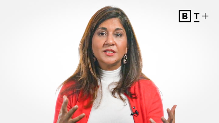 A woman with long brown hair wearing a red cardigan and white turtleneck speaks, gesturing with her hands, in front of a plain white background with a BT+ logo.