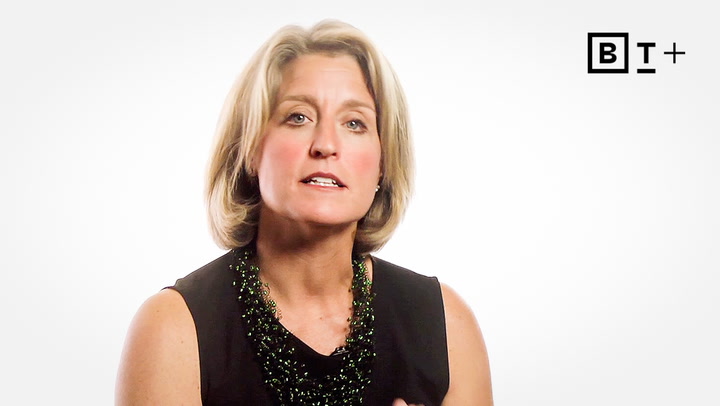 A woman with short blonde hair wearing a black sleeveless top and beaded necklace speaks in front of a white background with a “BT+” logo in the top right corner.