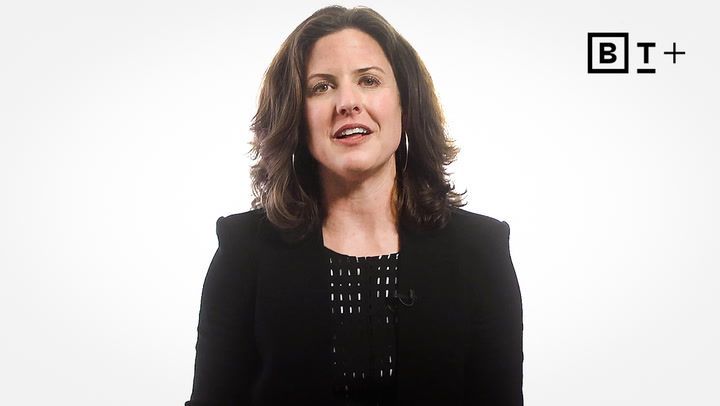 A woman with shoulder-length brown hair wearing a black blazer speaks in front of a white background with a "BT+" logo in the top right corner.