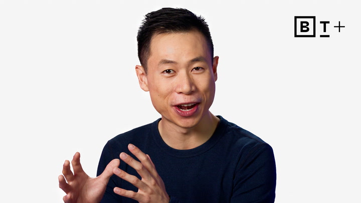 A man with short dark hair gestures with his hands while speaking. He is wearing a dark sweater and is set against a plain white background with a "BT+" logo in the top right corner.