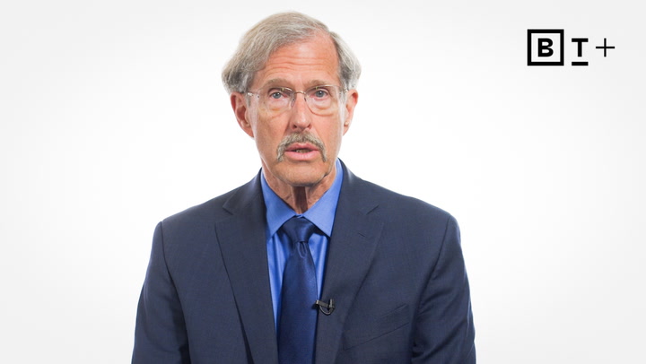 An older man with glasses, a mustache, and gray hair wearing a blue suit and tie speaks in front of a plain white background with a "BT+" logo in the top right corner.
