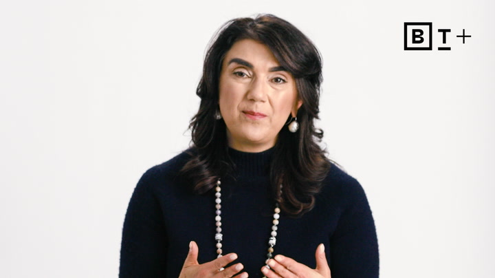 A woman with dark hair wearing a navy sweater and beaded necklace speaks while gesturing with her hands; BT Plus logo appears in the top right corner.