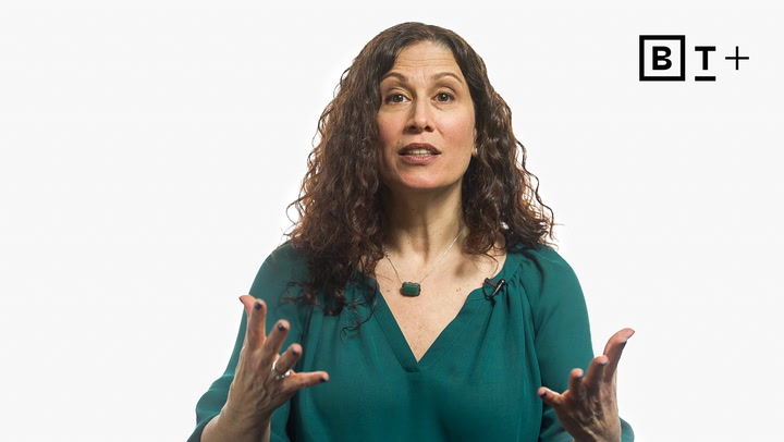 Woman with curly brown hair in a teal blouse gestures while speaking in front of a plain white background with a "BT+" logo in the upper right corner.