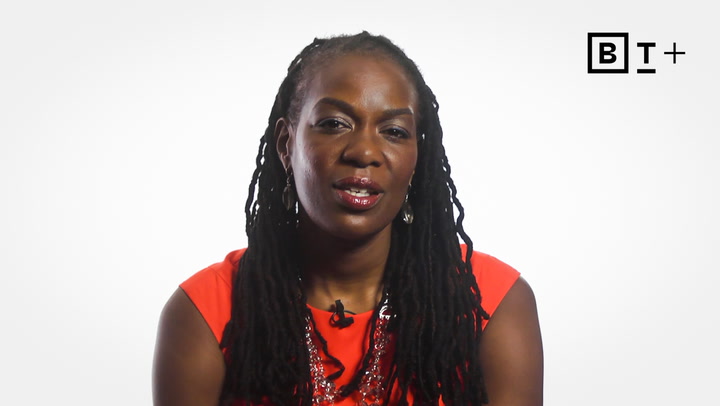 A woman with long braided hair wears a red top and necklace, sitting against a plain white background with the BT+ logo in the top right corner.