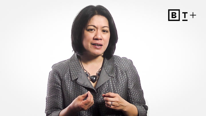 A woman in a patterned gray jacket speaks while gesturing with her hands. A "BT+" logo appears in the top right corner against a white background.