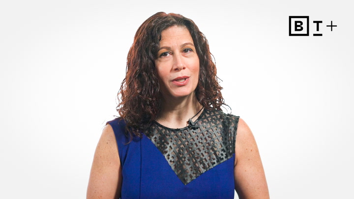 A woman with curly brown hair wearing a sleeveless blue top speaks in front of a plain white background with a "BT+" logo in the corner.