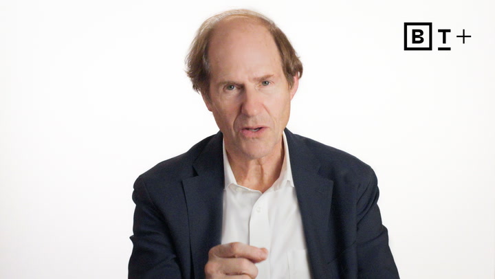 A middle-aged man in a dark blazer and white shirt speaks while gesturing, with a white background and a "B T +" logo in the top right corner.