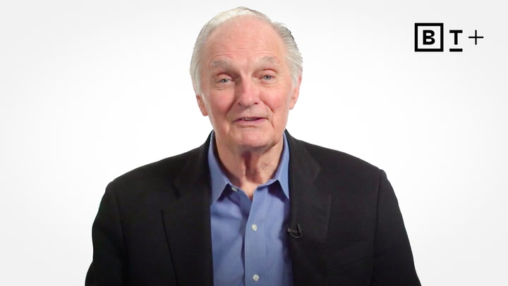 An older man in a dark blazer and blue shirt stands against a plain white background with the "B T +" logo in the top right corner.