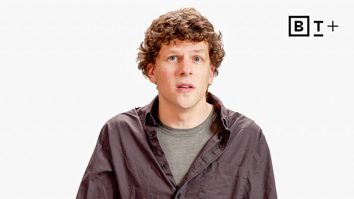A man with curly hair, wearing a gray t-shirt and dark button-up shirt, stands against a white background with a “B T +” logo in the top right corner.