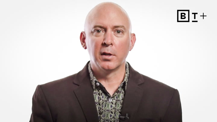 A bald man in a patterned shirt and dark blazer stands against a plain white background with a "BT+" logo in the top right corner.