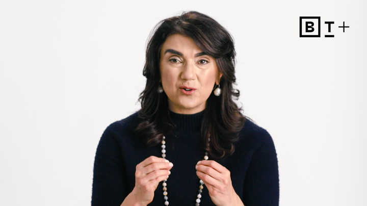 A woman with long dark hair and a navy sweater speaks while gesturing, with a BT+ logo in the top right corner against a plain white background.