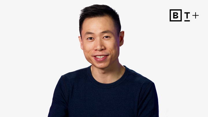 A person with short black hair and a navy blue shirt smiles at the camera, with a "B T +" logo in the top right corner on a plain white background.