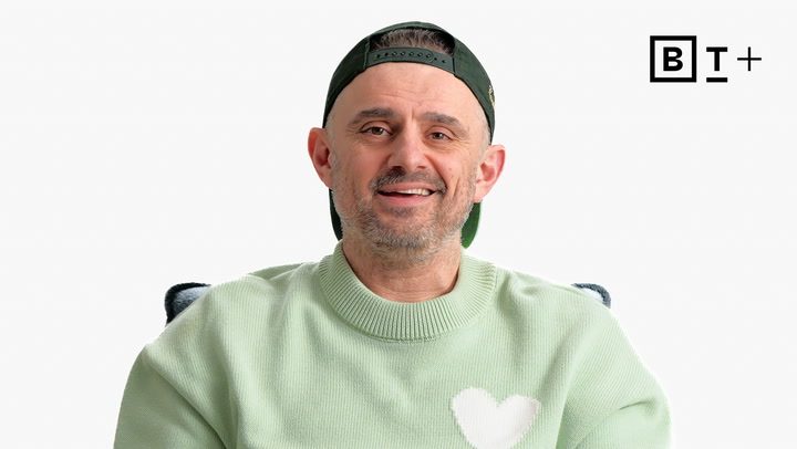 Man wearing a light green sweater with a white heart design and a backwards green cap, smiling at the camera; BT+ logo in the top right corner on a plain background.